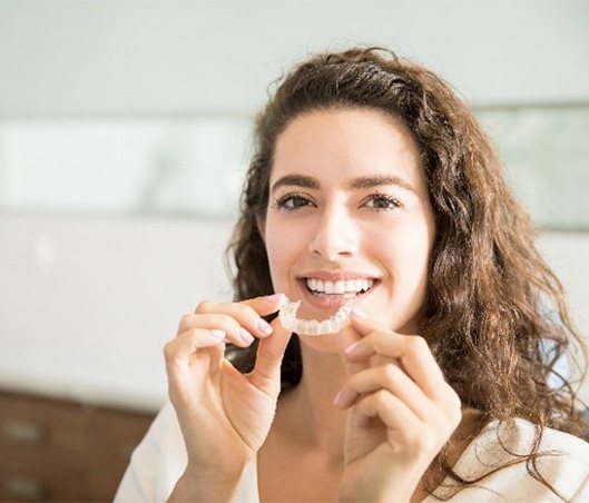 Woman smiling while holding clear aligner in her hands