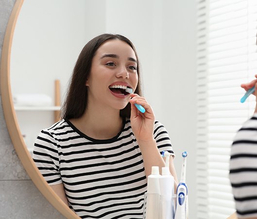 Woman in horizontally striped shirt brushing her teeth